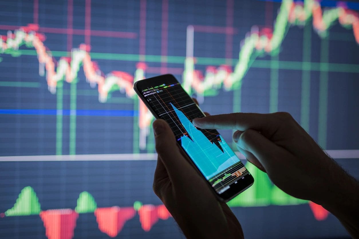 Person analyzing stock market data on a smartphone with charts in the background.